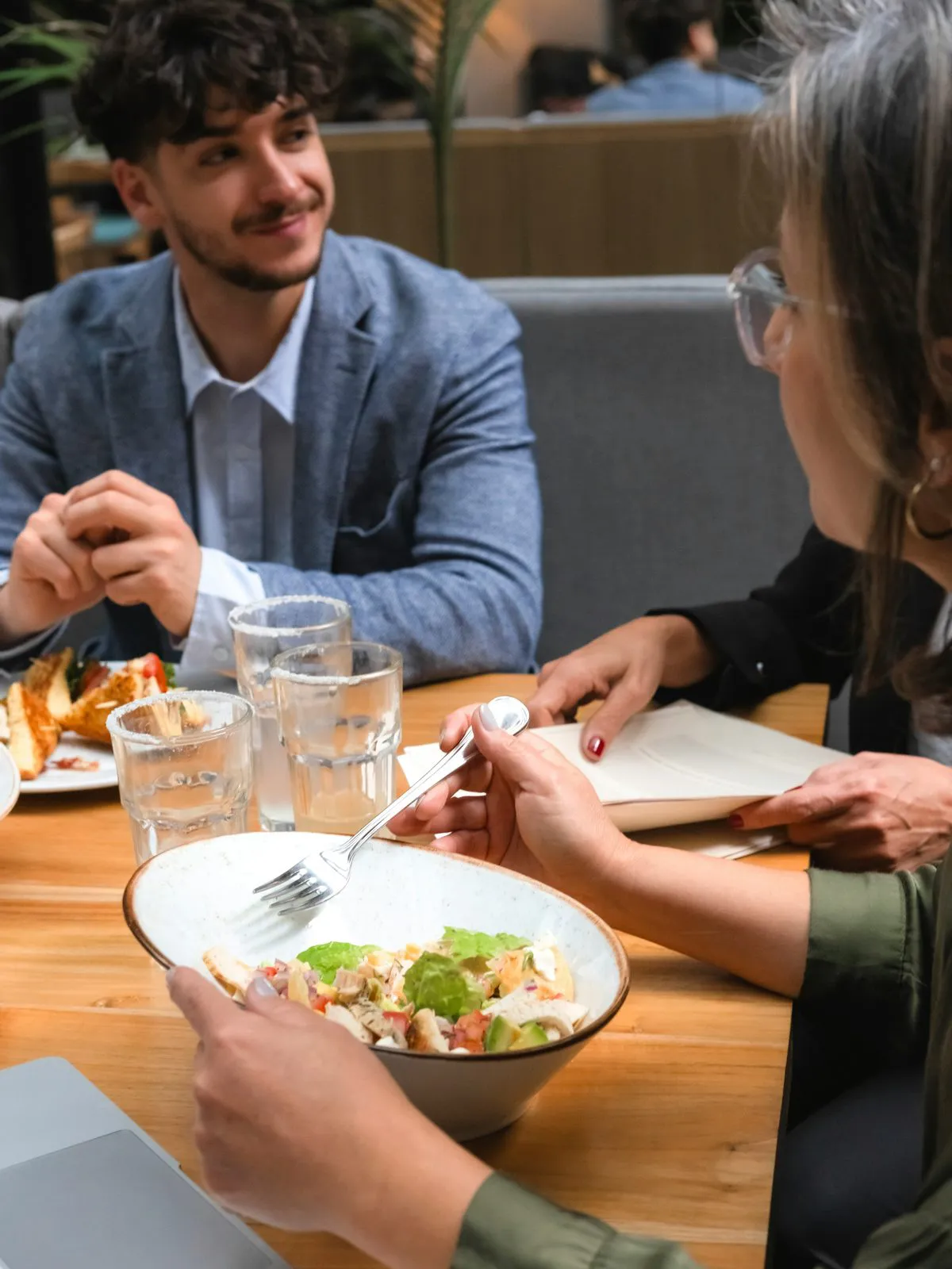 Goście restauracji rozmawiają przy stole nad sałatką i wodą